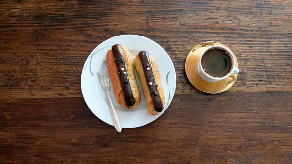 Tahta arka planda bir tabak ve bir fincan kahveyle iki ekler.