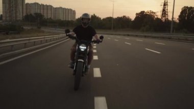 Gün batımında bir adam geniş bir otoyolda motosiklet sürüyor.