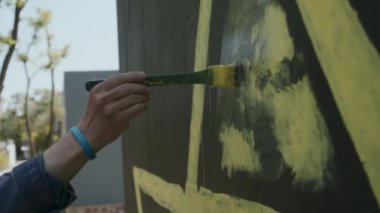 Bir adam gri bir duvara sarı bir üçgen çizer.