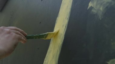 El, gri arkaplanda fırçayla sarı bir çizgi çizer.