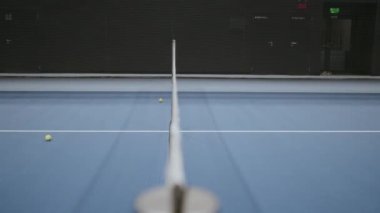 Mavi kortta siyah tenis ağı. Arka planda bir top zıplıyor