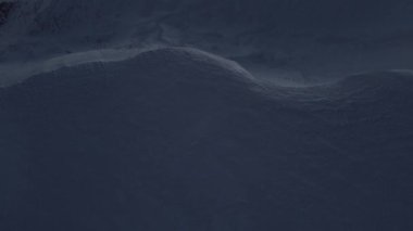 Yoğun karla kaplı bir ormana akan dağlık arazinin sinematik manzarası.