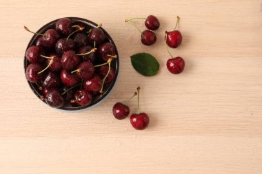 Tahta arka planda, ahşap bir kasede taze kirazlar. Üst görünüm, düz uzanma.