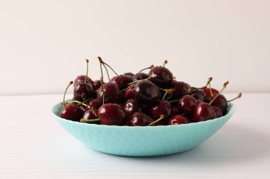 Kırmızı kirazlar mavi kasede, arka planda.