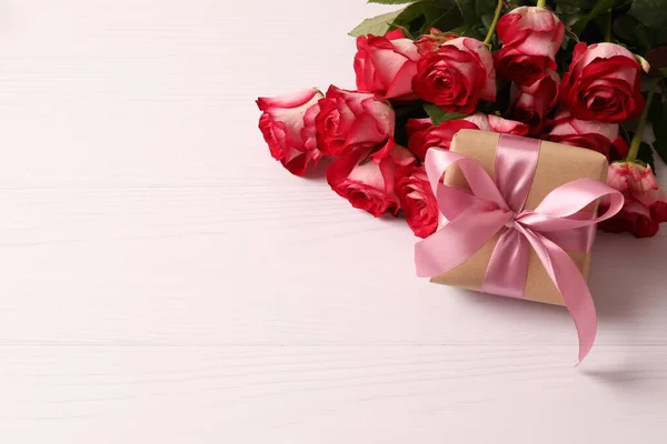 beautiful red roses and gift boxes on light wooden background, space for text