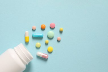 Beyaz kapsüllü renkli haplar ve mavi arka planda pembe haplar.
