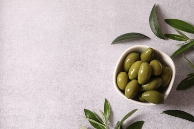 Gri arka planda yaprakları olan bir kase lezzetli zeytin.