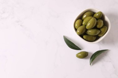 Bir kase yeşil zeytin ve gri mermer masada yapraklar