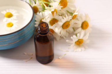 Cam şişe papatya çayı ve ahşap masa üzerinde papatya yağı.