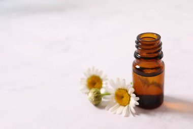 Beyaz tahta üzerinde gerekli yağ ve papatya çiçekleri olan bir şişe. alternatif tıp kavramı