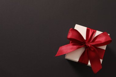 Gri arka planda kırmızı kurdeleli hediye kutusu.