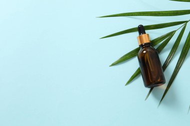 Renk arka planında taze yeşil yapraklar olan gerekli yağ şişesi. düz yat.