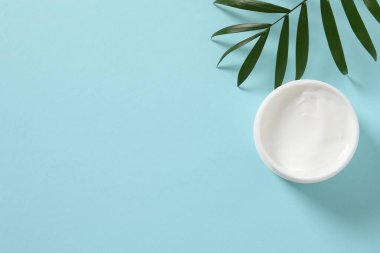Yapraklı beyaz kozmetik kavanoz ve mavi arka planda beyaz kağıt..