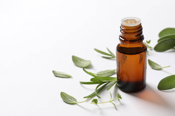 fresh essential oil in glass bottle and branch of fresh green leaves on white background.