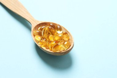 Omega-3 kapsüllerinin ahşap kaşığı mavi arka planda, kopyalanmış. Sağlık, refah ve takviyeler..