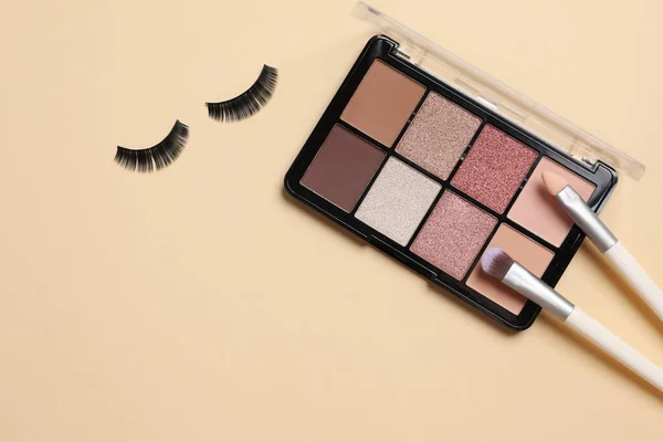Makeup palette with brushes and eyelashes on a colored background
