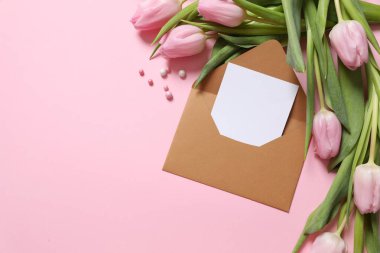 İçinde beyaz notlar olan el işi kağıt zarf ve renkli arka planda güzel laleler.