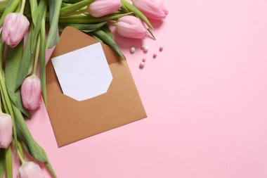 İçinde beyaz notlar olan el işi kağıt zarf ve renkli arka planda güzel laleler.