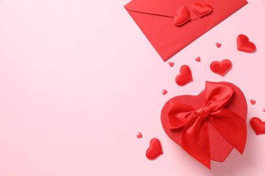 Kırmızı kağıt zarf ve pembe arka planda kalpleri olan hediye. Düz yatış, üst görünüm