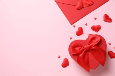 Kırmızı kağıt zarf ve pembe arka planda kalpleri olan hediye. Düz yatış, üst görünüm
