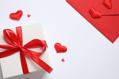 Kırmızı zarfta hediye ve pembe arka planda kırmızı kalpler. Düz yatış, üst görünüm