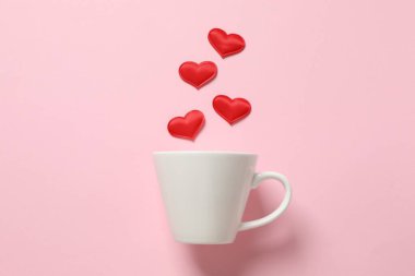 Renkli arka planda kırmızı kalpleri olan beyaz bardak.