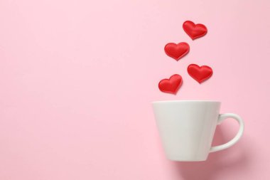 Renkli arka planda kırmızı kalpleri olan beyaz bardak.