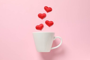 Renkli arka planda kırmızı kalpleri olan beyaz bardak.