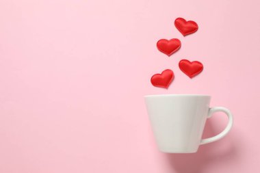 Renkli arka planda kırmızı kalpleri olan beyaz bardak.