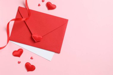 Kırmızı kağıt zarf ve pembe arka planda kırmızı kalpler. Düz yatış, üst görünüm