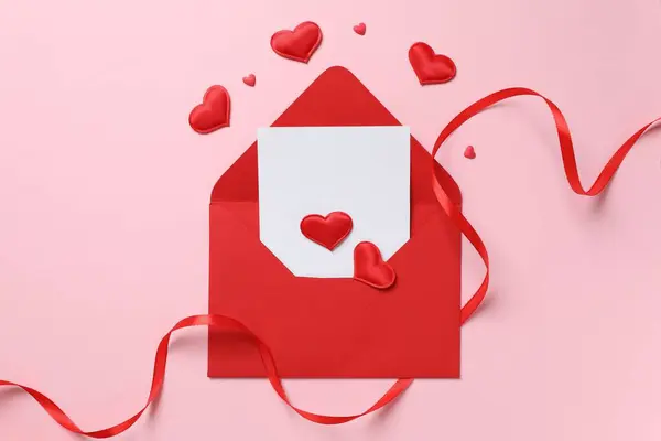 Red paper envelope and red hearts on pink background. Flat lay, top view