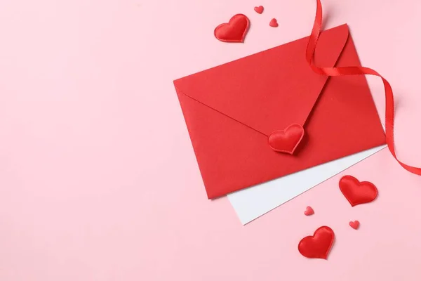 Red paper envelope and red hearts on pink background. Flat lay, top view