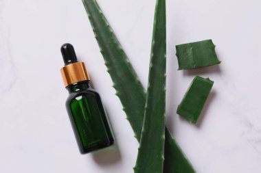 Gri arka planda taze aloe vera yapraklı düz kozmetik serumu. Organik kozmetik ürünleri. Üst görünüm düzlüğü, kopyalama alanı. Kozmetik, SPA markalaşması, maket.