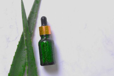 Gri arka planda taze aloe vera yapraklı düz kozmetik serumu. Organik kozmetik ürünleri. Üst görünüm düzlüğü, kopyalama alanı. Kozmetik, SPA markalaşması, maket.