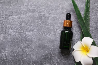 Gri arka planda taze aloe vera yapraklı düz kozmetik serumu. Organik kozmetik ürünleri. Üst görünüm düzlüğü, kopyalama alanı. Kozmetik, SPA markalaşması, maket.