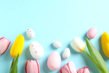 Paskalya dekoru konsepti. Pastel arka planda lale çiçekleri olan renkli yumurtaların en üstteki fotoğrafı 