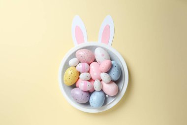 Paskalya dekoru konsepti. Renkli yumurtaların renkli bir tabakta, pastel arka planda tavşan kulaklı bir fotoğrafı. 