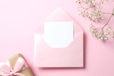 Üzerinde kağıt kart, hediye ve pastel pembe arka planda beyaz çigila çiçekleri olan açık pembe zarfın en üstteki fotoğrafı.