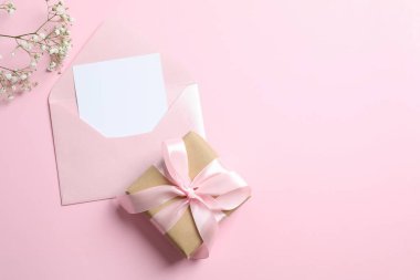 Düğün davetiyesi konsepti. Üzerinde kağıt kart, hediye ve pastel pembe arka planda beyaz çigila çiçekleri olan açık pembe zarfın en üstteki fotoğrafı.