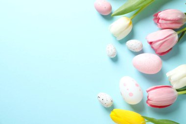 Paskalya dekoru konsepti. Renkli arkaplanda lale çiçekleri olan renkli yumurtaların en üstteki görüntüsü