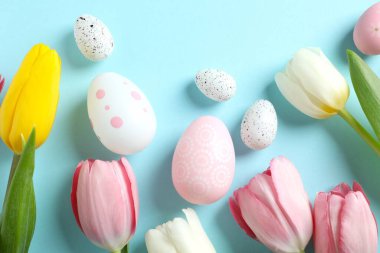 Paskalya dekoru konsepti. Renkli arkaplanda lale çiçekleri olan renkli yumurtaların en üstteki görüntüsü