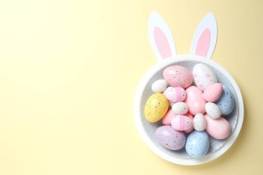 Paskalya dekoru konsepti. Renkli yumurtaların renkli bir tabakta, pastel arka planda tavşan kulaklı bir fotoğrafı.