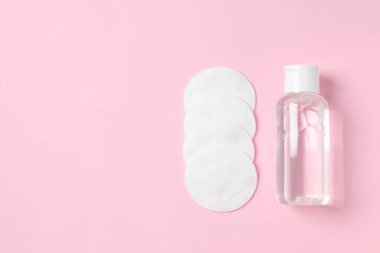 Renk arkaplanına Micellar temizleme suyu ve pamuk pedleri, üst görünüm.