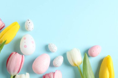 Paskalya dekoru konsepti. Renkli arkaplanda lale çiçekleri olan renkli yumurtaların en üstteki görüntüsü