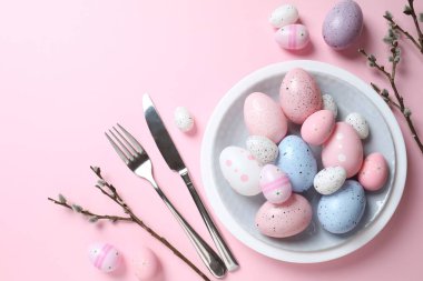 Paskalya dekoru konsepti. Renkli yumurtaların üst görüntüsü tabaktaki çatal ve bıçakla pastel arka planda.