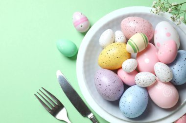 Paskalya dekoru konsepti. Renkli yumurtaların üst görüntüsü tabaktaki çatal ve bıçakla pastel arka planda.