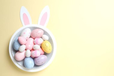 Paskalya dekoru konsepti. Renkli yumurtaların renkli bir tabakta, pastel arka planda tavşan kulaklı bir fotoğrafı.