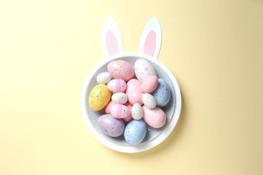 Paskalya dekoru konsepti. Renkli yumurtaların renkli bir tabakta, pastel arka planda tavşan kulaklı bir fotoğrafı.