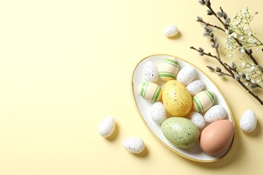 Paskalya dekoru konsepti. Pastel arka planda çiçekli bir tabakta renkli yumurtaların en üstteki fotoğrafı.