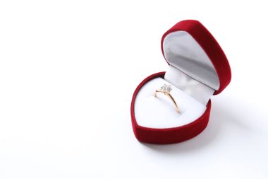 Güzel, parlak, altın bir nişan yüzüğü. Beyaz arka planda kırmızı kadife bir kutuda büyük bir elmas mücevher var.